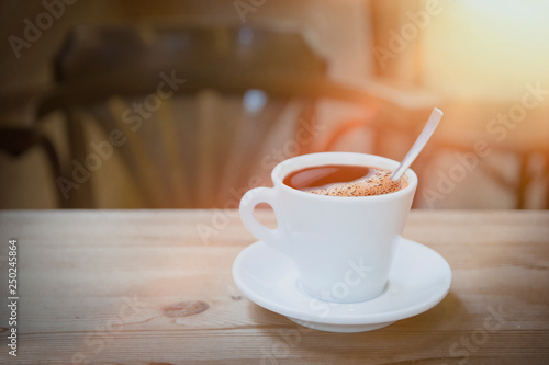 Cup of espresso coffee on a wooden table against a sun flare light. Empty copy space for Editor's text.