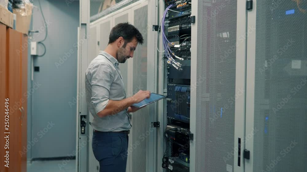 Server IT Engineer In Data Center Server Room.Network Engineer Working Laptop Computer.Server Rack Room Works.Programmer Checks A work Of Server At A Data Center. Server IT Engineer In Data Center Server Room.Network Engineer Working Laptop Computer.Server Rack Room Works.Programmer Checks A work Of Server At A Data Center.