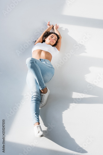 Fototapeta Naklejka Na Ścianę i Meble -  Joyful girl in crop top and jeans lying on floor with smile