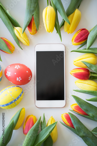Fototapeta Naklejka Na Ścianę i Meble -  easter, holidays, tradition and object concept - smartphone with colored eggs and tulip flowers on white background