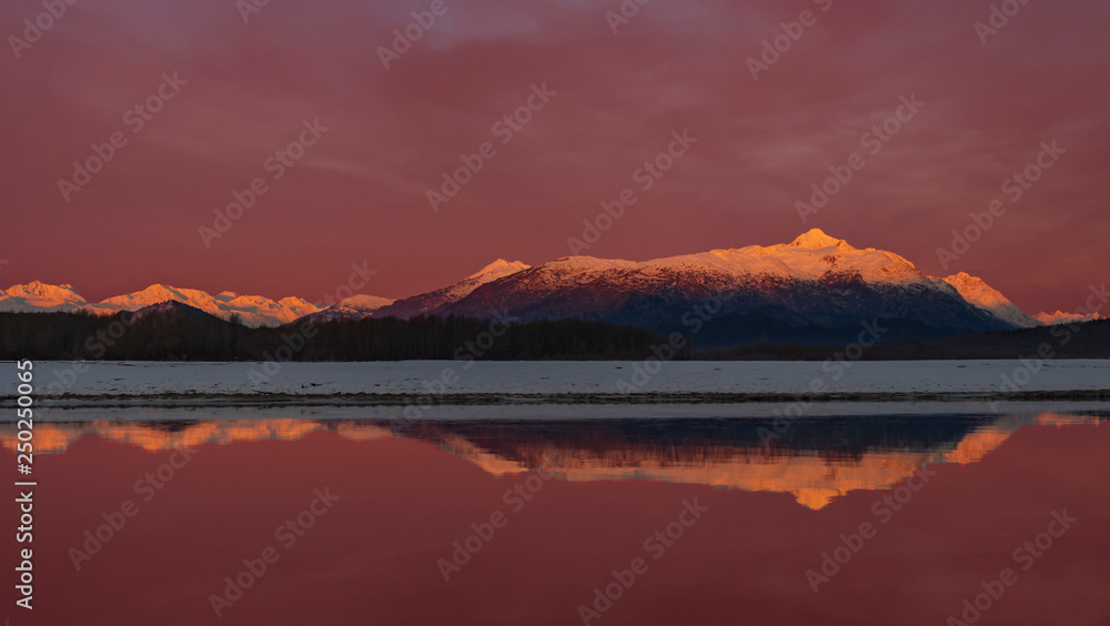Fototapeta premium Chilkat Reflection - The Chilkat Mountain Range in Alpen Glow is reflected in the smooth flowing waters of the Chilkat river at sunrise. Haines, Alaska, 