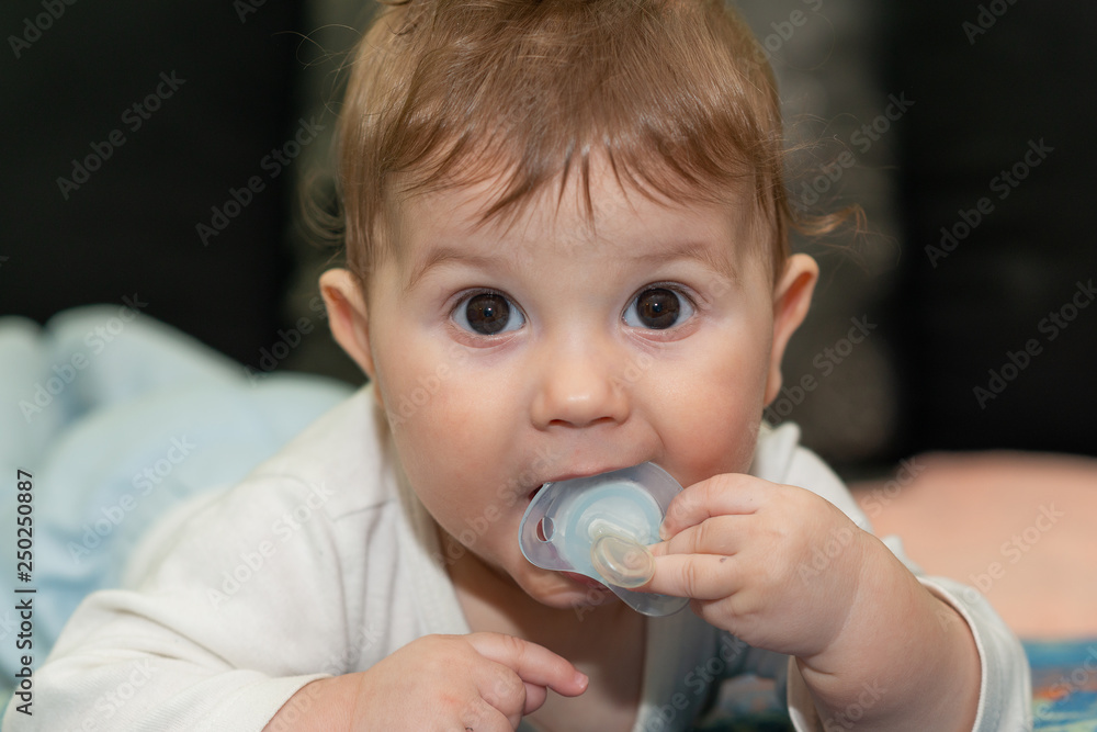 Baby boy is lying on tummy. The baby boy poses and plays with a pacifier. Baby boy is lying on tummy. The baby boy poses and plays with a pacifier.