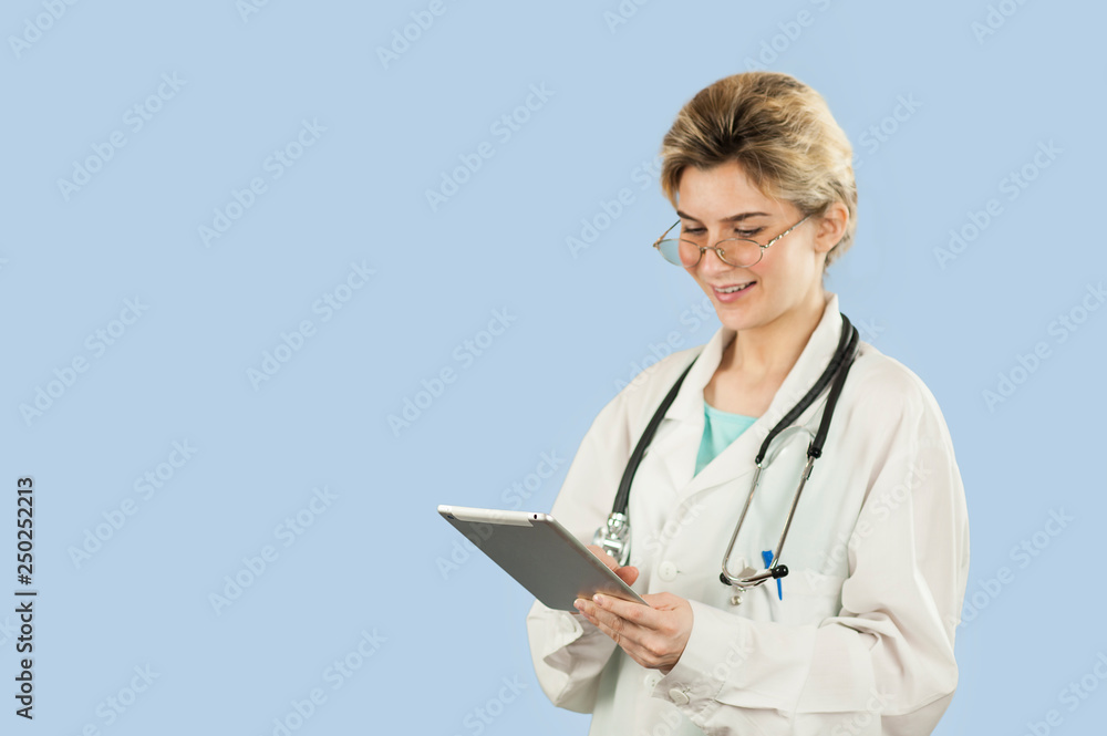 beautiful girl doctor with a computer in her hands is looking for information on a blue isolated background. The concept of health and modern medical network technologies beautiful girl doctor with a computer in her hands is looking for information on a blue isolated background. The concept of health and modern medical network technologies