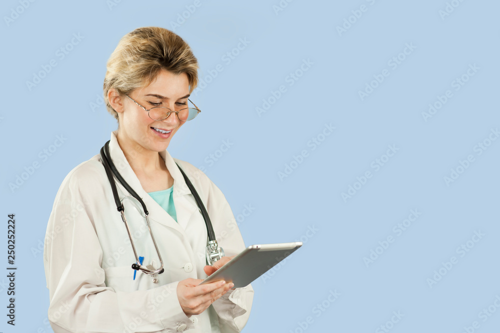 beautiful girl doctor with a computer in her hands is looking for information on a blue isolated background. The concept of health and modern medical network technologies beautiful girl doctor with a computer in her hands is looking for information on a blue isolated background. The concept of health and modern medical network technologies