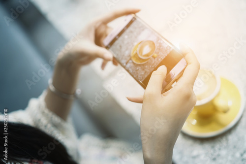 Woman taking photo of cup of coffee on her smartphone for social netmedia at a coffee shop.