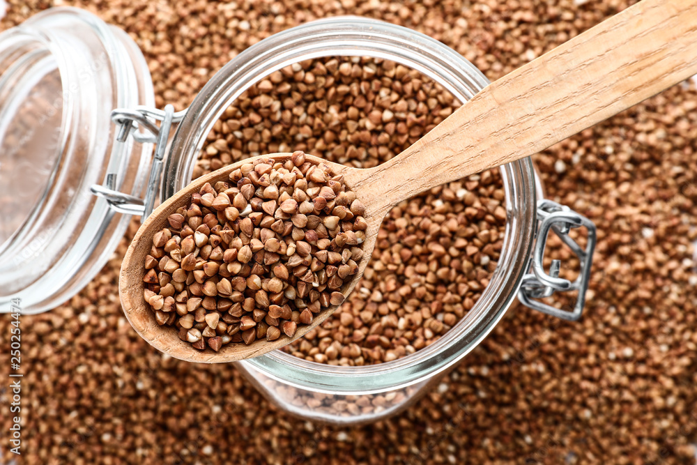 Glass jar and spoon with raw buckwheat, top view Glass jar and spoon with raw buckwheat, top view