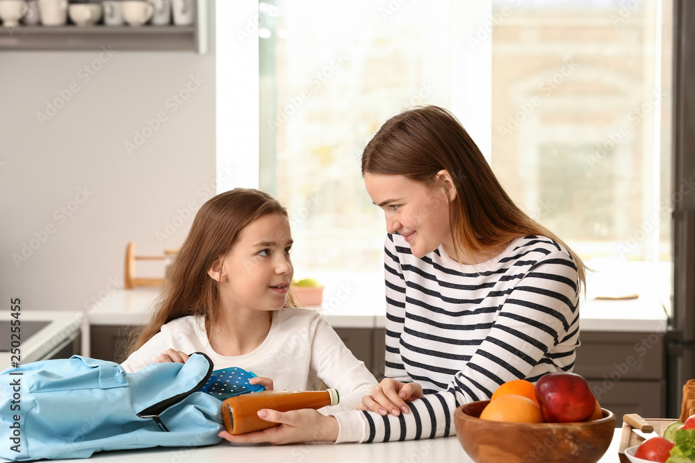 Mother putting lunch box into backpack of her little daughter before school Mother putting lunch box into backpack of her little daughter before school