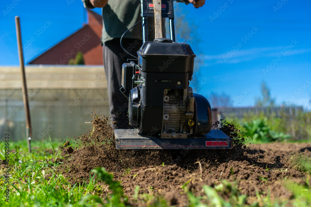 The cultivator loosens the ground. The farmer works with a motor-block The cultivator loosens the ground. The farmer works with a motor-block