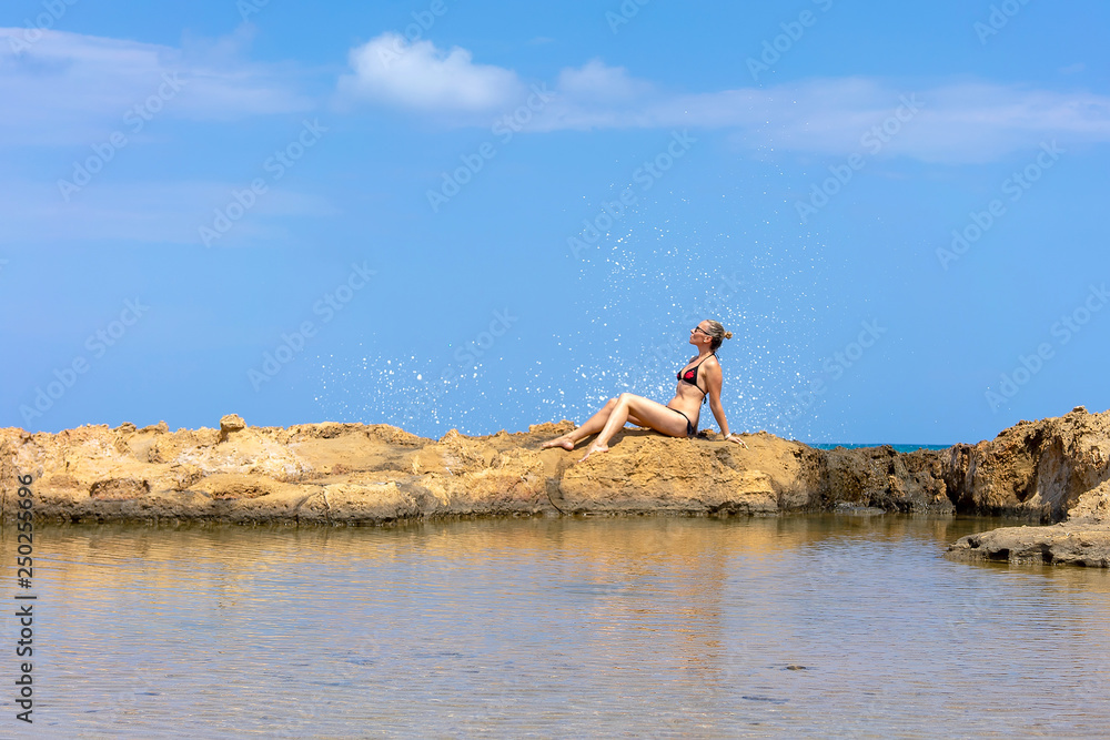 Girl posing sitting on the stones against the backdrop of the splashing sea