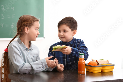 Photography Little boy sharing his school lunch with girl in classroom