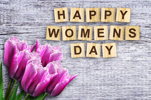 Happy womens day, the inscription consists of the alphabet on wooden cubes. Beautiful tulips. Wooden background.