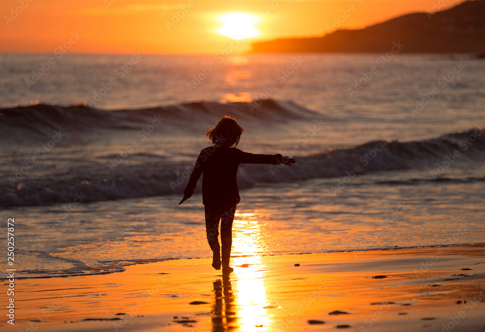 Happy child running on the beach during sunset, Praia da Luz, Algarve, Portugal