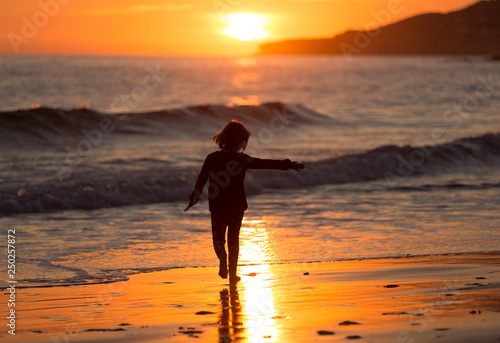 Happy child running on the beach during sunset, Praia da Luz, Algarve, Portugal