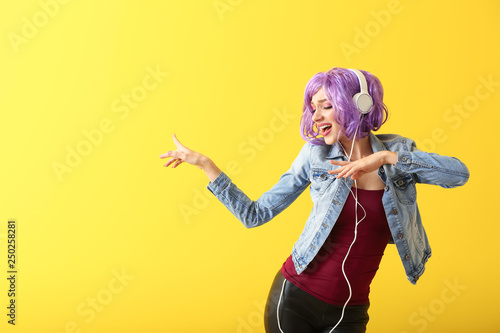 Beautiful young woman with headphones dancing against color background