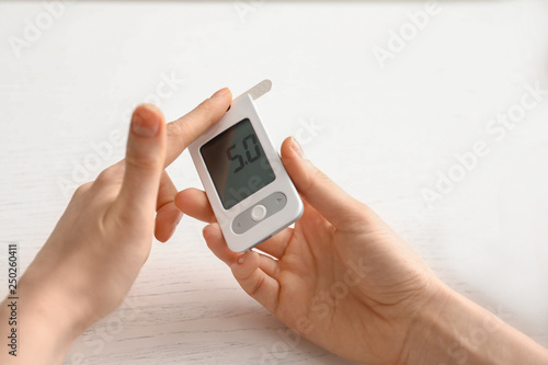 Diabetic woman measuring blood sugar level with digital glucometer at home, closeup