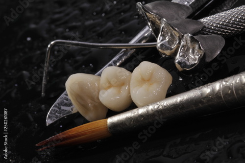 E-max pressed ceramic bridge and metal crown with dentistry utensils on wet surface