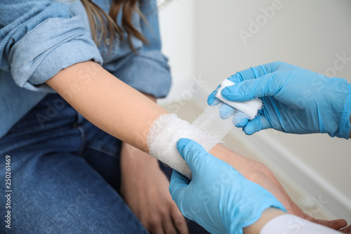 Leinwand Poster Doctor applying bandage onto wrist of young woman, closeup