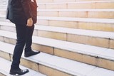 modern businessman hand holding briefcase beside working close up legs walking up the stairs in modern city. in rush hour to work in office a hurry. During the first morning of work. stairway