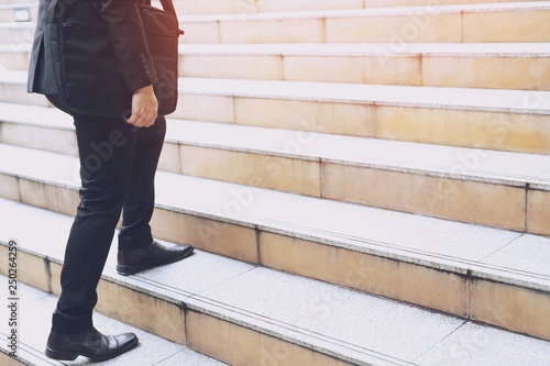 modern businessman hand holding briefcase beside working close up legs walking up the stairs in modern city. in rush hour to work in office a hurry. During the first morning of work. stairway