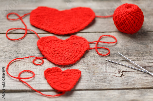 Three red knitted hearts on a gray wooden background  symbolizing love and family. Family relationship  bonds.