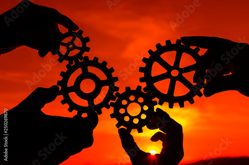 gears in the hands of people at sunset. the mechanism of teamwork. interactions