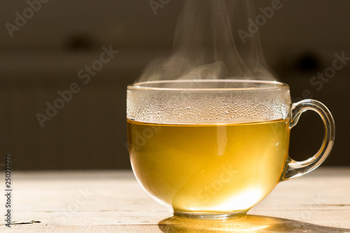 Steaming hot tea in glass mug on a wooden table. Refreshing morning image with a tea cup in back lighting.