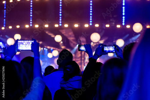 Silhouettes of crowds of spectators at a concert with smartphones in their hands.