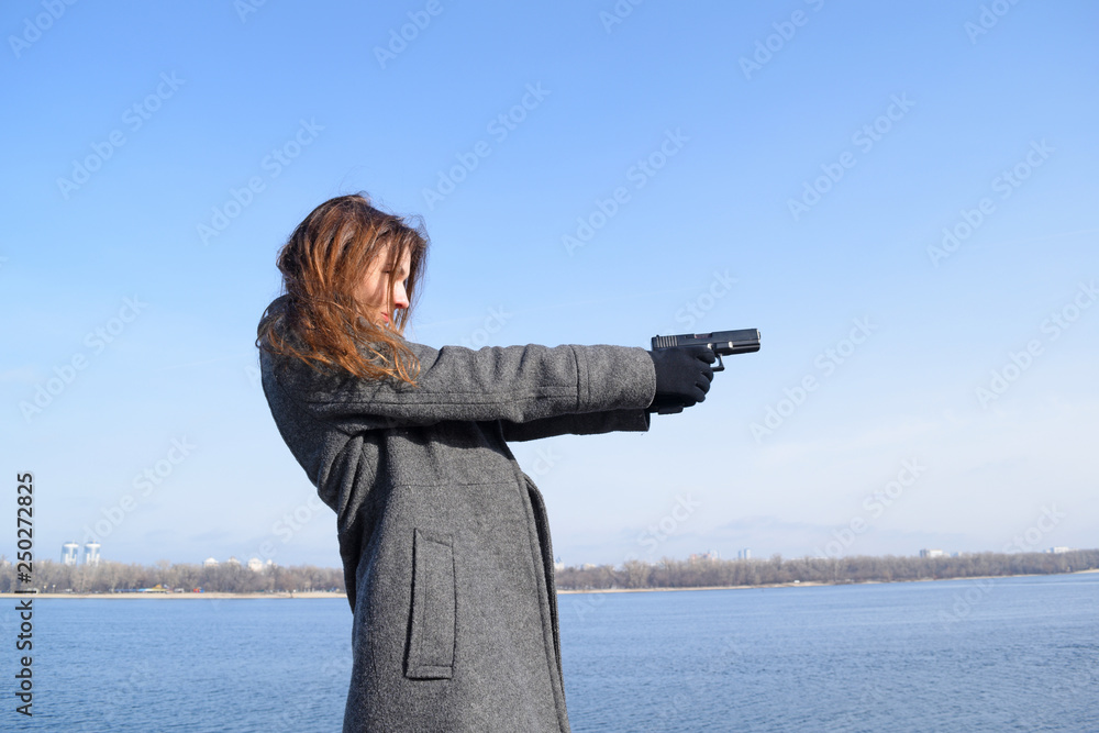 Obraz premium A young girl in a coat shoots with a gun near the river in the city.
