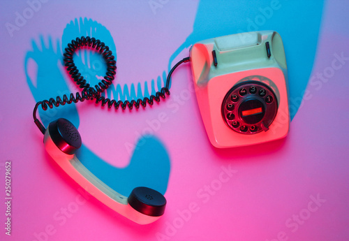 Vintage rotary phone. Retro wave, pink blue neon light, ultraviolet. Top view, minimalism