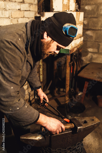 Blacksmith forges a hot metal on the anvil with a hammer.