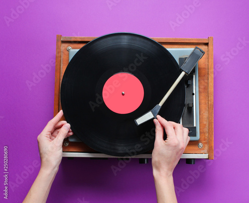 Female hands set up retro vinyl record player with plate on purple background. Top view