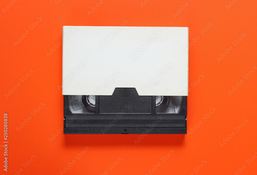The videotape in a paper case on orange background. Pop culture attributes, minimalism. Top view The videotape in a paper case on orange background. Pop culture attributes, minimalism. Top view