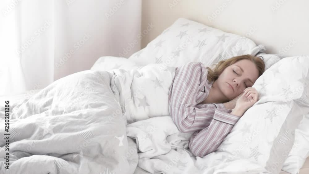 Beautiful young Woman is Sleeping on white Pillow. Girl in Pajamas is Waking up. Caucasian Female on Bed early in Morning. Beautiful young Woman is Sleeping on white Pillow. Girl in Pajamas is Waking up. Caucasian Female on Bed early in Morning.