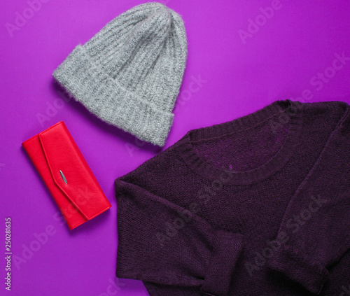 Women's fashion items on a purple background. Sweater, warm hat, red purse. Top view