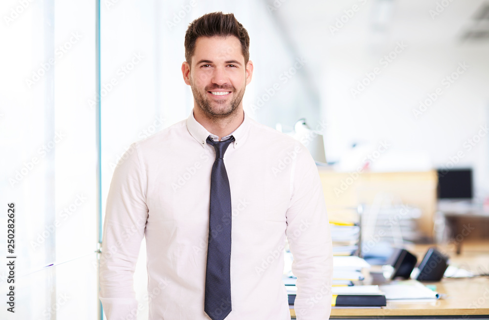 Portrait of businessman standing in the office while smiling and looking at camera Portrait of businessman standing in the office while smiling and looking at camera