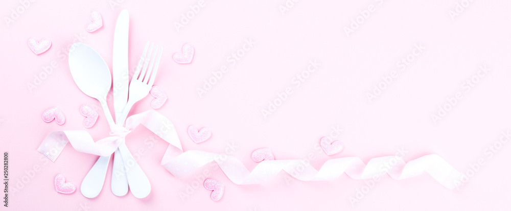 Festive table setting for Valentines Day with fork, knife and hearts  on pink pastel background.Romantic dinner. Space for text. Top view.Banner