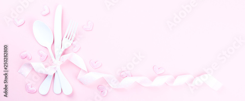 Festive table setting for Valentines Day with fork, knife and hearts  on pink pastel background.Romantic dinner. Space for text. Top view.Banner © lily_rocha