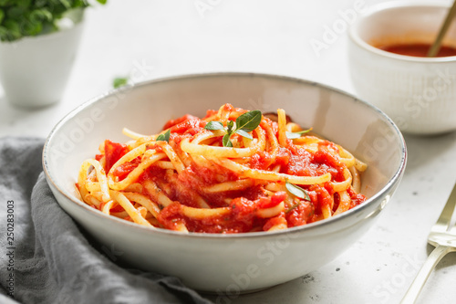 Traditional pasta with tomato and Greek basil sauce in a ceramic bowl on a white table.