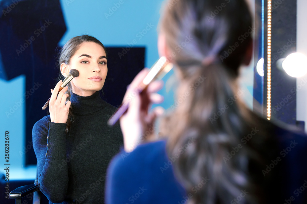 Beautiful young woman using brush while applying her makup
