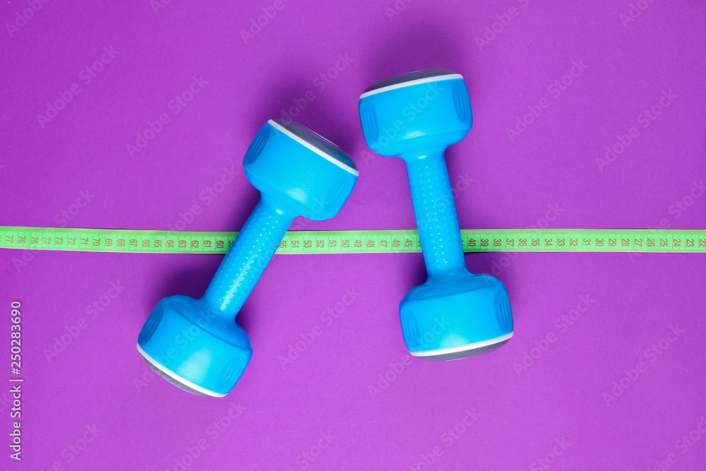 The concept of losing weight. Blue plastic dumbbells, ruler on purple background. Sport, fitness. Top view. Flat lay The concept of losing weight. Blue plastic dumbbells, ruler on purple background. Sport, fitness. Top view. Flat lay