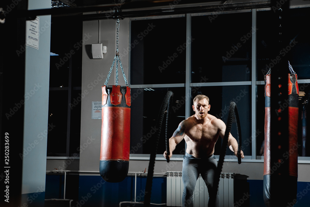 Strong man posing in gym with ropes