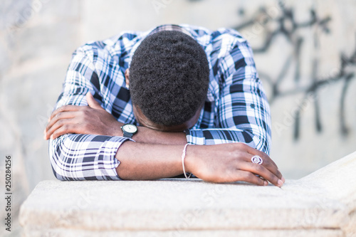 Black african man desperate with down head on arms crying - sadness concept for diversity male in outdoor