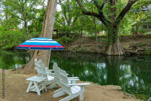 White adirondack lounge chairs and a colorful sun umbrella for relaxing on a summer day at Cypress Creek  a public park in Wimberley Texas photo