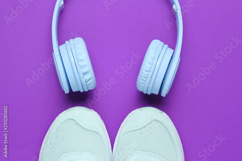 Blue wireless headphones, sneakers on a purple background. Top view