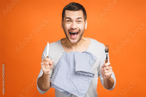 Young hungry crazy man holding a fork and a knife. Isolated on orange background. photo