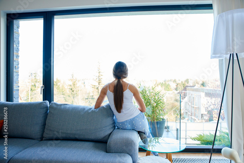 Young woman looking out the window while relaxing on the sofa