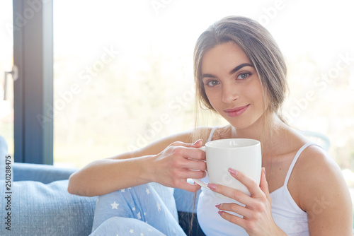 Beautiful young woman holding mug in her hand while relaxing on sofa at home