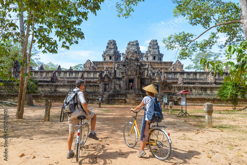 Tourist couple cycling around Angkor temple, Cambodia. Ta Keo building ruins in the jungle. Eco friendly tourism traveling, toned image. © fabio lamanna