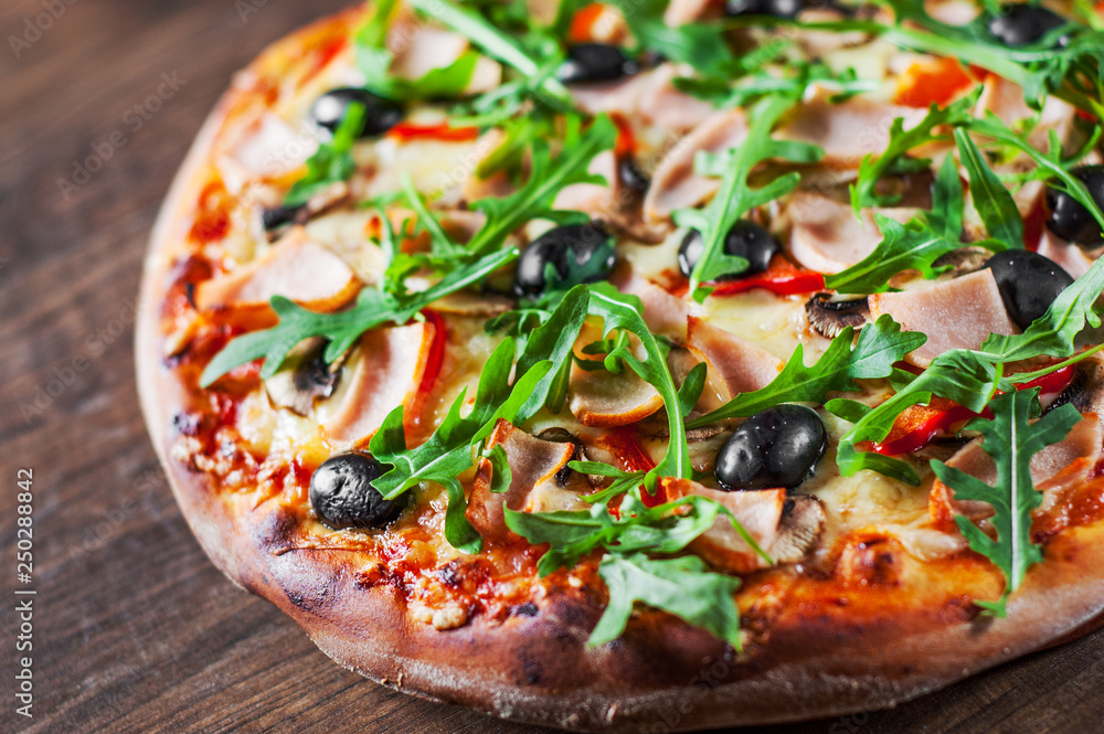Pizza with Mozzarella cheese, mushrooms, ham, tomato sauce, pepper, olives, Spices and Fresh arugula. Italian pizza on wooden table background Pizza with Mozzarella cheese, mushrooms, ham, tomato sauce, pepper, olives, Spices and Fresh arugula. Italian pizza on wooden table background