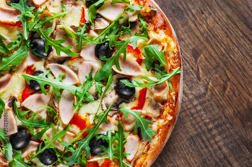 Pizza with Mozzarella cheese, mushrooms, ham, tomato sauce, pepper, olives, Spices and Fresh arugula. Italian pizza on wooden table background